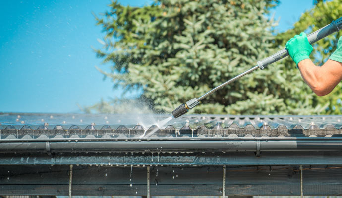 Person cleaning gutter with equipment