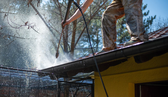 A person using a pressure washer to clean the gutters