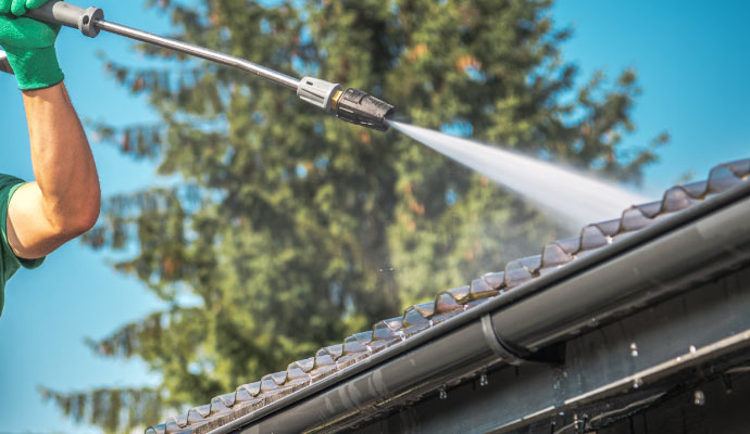 A person using a pressure washer to clean a gutter