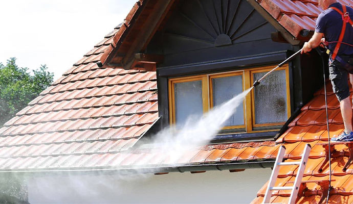 A man is softwashing roof gutter