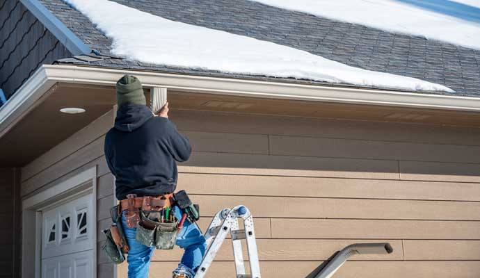 A person is repairing a downspout attached to the side of a house.