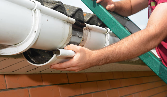 Person repairing a white gutter on a house roof