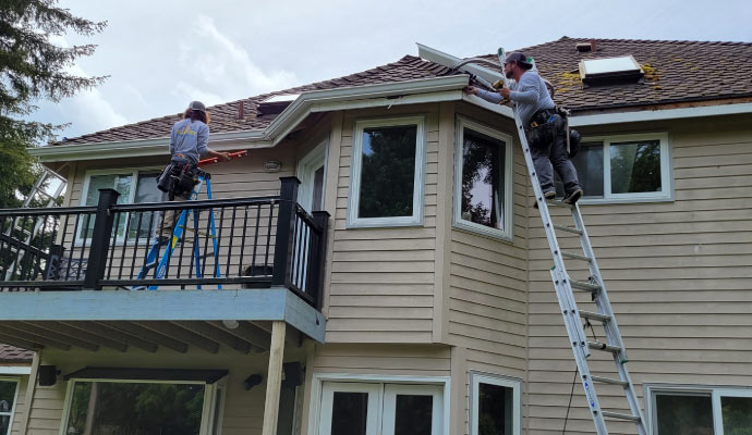 two individuals working on replacing a gutter from a house